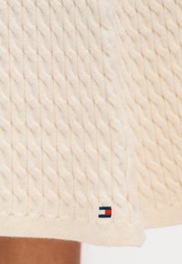 Πλεκτό πουλόβερ σε εκρού απόχρωση με υφή καναλιού. Διαθέτει μικρό, επώνυμο διακοσμητικό σε κόκκινο, άσπρο και μπλε στο τελείωμα.