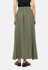 Lunga gonna verde oliva realizzata in tessuto leggero, con vita elasticizzata, caratterizzata da una silhouette fluida e un orlo che sfiora il terreno.