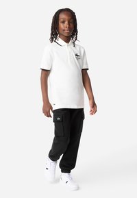 Biely polo tričko s krátkymi rukávmi a čiernym lemovaním, skombinované s čiernymi cargo nohavicami s prednými vreckami a bielymi teniskami.