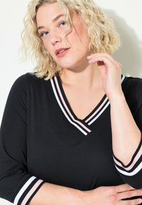 Černý top s výstřihem do V a pruhovaným výstřihem v bílé a růžové barvě, 3/4 rukávy se sladěnými pruhy, vyrobený z měkkého materiálu.