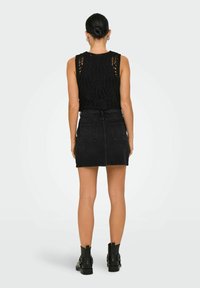 Zwarte haakwerk tanktop gecombineerd met een hooggesneden zwarte denim minirok, voorzien van riemlussen en achterzakken. Zwarte enkellaarsjes maken de look compleet.