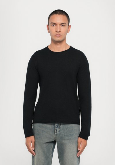 Pull en tricot noir à manches longues avec un col rond, présentant une texture lisse et une coupe ajustée, associé à un jean en denim bleu clair.