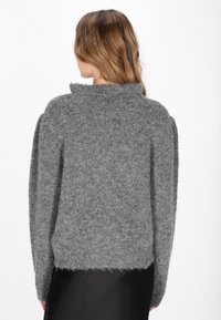 Grijze gebreide trui met een hoge kraag, oversized pasvorm en een gestructureerde afwerking. Lange mouwen en een losse, cropped zoom maken het ontwerp compleet.