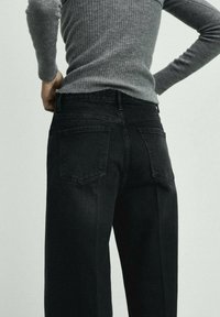 Jeans neri con una vestibilità affusolata, dotati di due tasche posteriori e una texture sottile. Abbinati a un maglione grigio a coste.