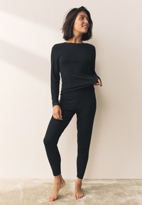 Top negro de manga larga con textura acanalada y detalles de encaje, combinado con pantalones ajustados a juego, ambos en un tejido suave y elástico.