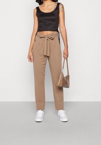 Czarna przyszywana koszulka na ramiączkach, beżowe spodnie z wysokim stanem i zawiązanym paskiem, białe trampki oraz mała błyszcząca brązowa torebka.