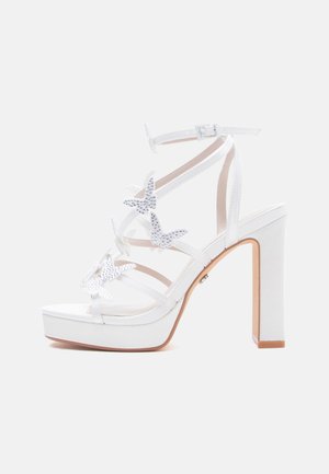Sandalia blanca de plataforma con tacón alto, tira en el tobillo y detalles decorativos de mariposas de estrás en varias correas frontales.