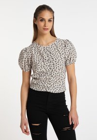 Bluse med blomsterprint, korte puffærmer, rund hals og tekstureret overflade. Bæres med sorte slidte jeans.