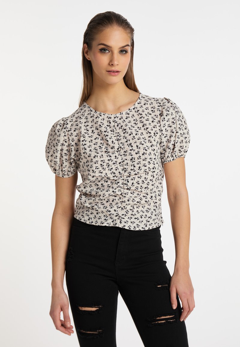 Blus med blommönster, korta puffärmar, rund hals och texturerad yta. Bärs tillsammans med svarta slitna jeans.