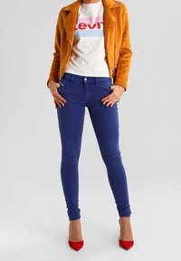 Modré skinny džíny spárované s bílým tričkem Levi's a hořčicově žlutou sukní, doplněné červenými vysokými podpatky.