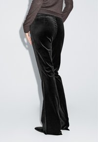 Svarträv sammet utsvängda byxor har en slät textur och sidoseam. Designen inkluderar en figurnära midja och en subtil glans.