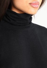 Pull à col roulé noir en tissu doux avec un col plié. Présente un design ajusté et une texture lisse, idéal pour les superpositions.