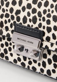 Torba s uzorkom leopard kože s crnim kožnim detaljima, koja ima srebrnu kopču s imenom brenda "MICHAEL KORS" istaknuto prikazanim.