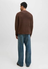 Bruine, gestructureerde gebreide trui, oversized pasvorm, gecombineerd met lichtblauwe, wijde denim broek. Minimaal detail, met overal effen kleuren.