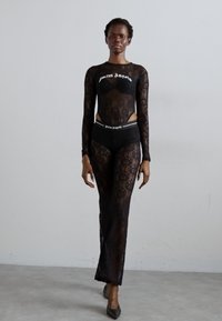 Schwarzer Spitzenbody mit langen Ärmeln, der ein kurzes Design und komplexe Muster aufweist. Kombiniert mit passendem schwarzen High-Waist-Unterwäsche.