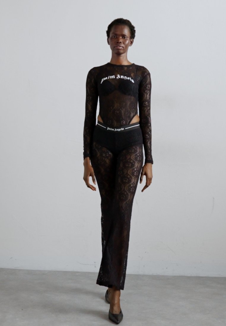 Bodysuit en dentelle noire à manches longues, présentant un design court et des motifs complexes. Associé à un sous-vêtement noir taille haute assorti.