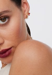 Złote kolczyki z prostokątnym przezroczystym kamieniem i owalnym czerwonym kamieniem, charakteryzujące się eleganckim wzornictwem i wypolerowanym wykończeniem.