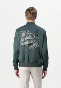 Green satin bomber jacket featuring a detailed embroidered mountain and floral design on the back, with a ribbed collar and cuffs.