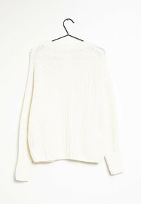 Maglione bianco a maglia appeso a un gancio nero, con una texture a coste, maniche ampie e una vestibilità rilassata con scollatura rotonda.