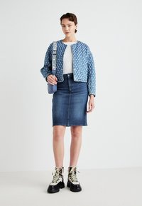 Blauwe jasje met patroon en ronde halslijn, witte blouse eronder, denim kokerrok en stevige zwart-witte laarzen met gele veters.
