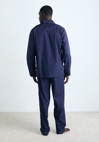 Ensemble de pyjama deux pièces bleu marine en coton avec une coupe droite. Présente des accents colorés sur le col et les poignets.