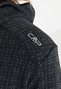 Close-up van een donkere, gemarmerde stof op de schouder van een jack met witte geborduurde letters "DWP."