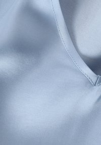 Helles bläuliches Satin-Gewebe, glatte Textur, mit einer gewölbten Kante und sichtbaren Steppnähten. Sanfter Glanz und fließendes Aussehen.