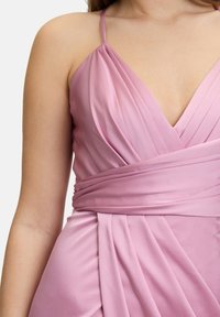 Robe en satin rose avec un décolleté plongeant, un design plissé et une taille enveloppée, ornée de délicates bretelles spaghetti.