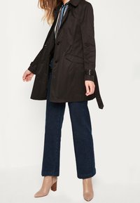 Czarny płaszcz trench z paskiem, czterema guzikami i bocznymi kieszeniami. Zestawiony z ciemnoniebieskimi spodniami typu wide-leg i beżowymi botkami na obcasie.