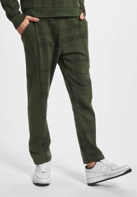 Grønne joggebukser med et svart geometrisk mønster, laget av mykt stoff, med sidelommer og en avslappet passform, kombinert med hvite sneakers.
