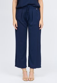 Marineblauwe wijde broek gemaakt van lichtgewicht stof met een hoge taille, plooien en een strikceintuur. Afgewerkt met subtiele gouden accenten.