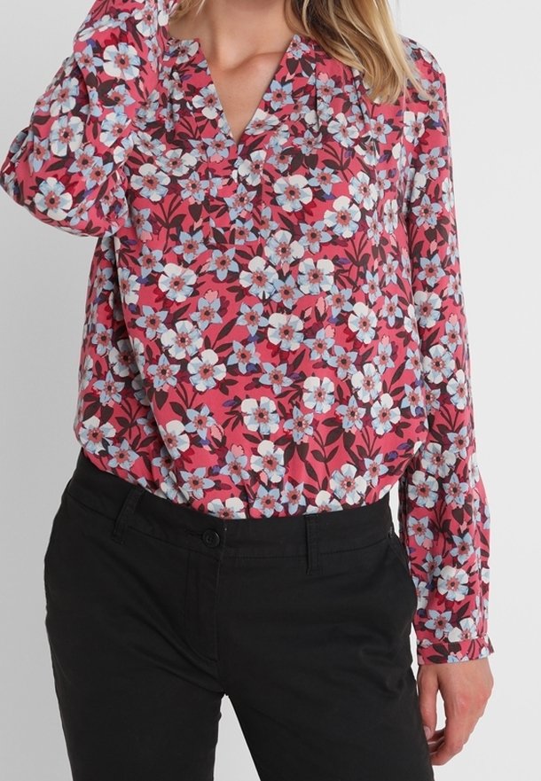 Pink floral blouse featuring a v-neck, long sleeves, and a pattern of white and blue flowers with green leaves, paired with black pants.
