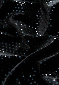 Tissu noir avec une surface texturée, présentant des points métalliques brillants aux nuances de bleu et d'argent variées, créant un motif ludique.