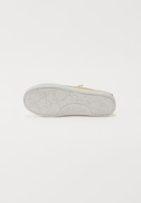 Chaussure jaune avec une tige texturée, dotée d'une semelle en caoutchouc blanc. La semelle présente un motif floral en relief et un logo de la marque.