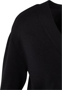 Pull noir en tricot avec un col en V, des manches longues et une finition texturée. Le matériau semble doux et léger.
