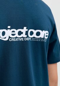 Tamnoplava pamučna majica s bijelim natpisom "project core CREATIVE DEPT. UNLIMITED EDITION." Mekana tekstura, klasičan dizajn s kružnim izrezom.