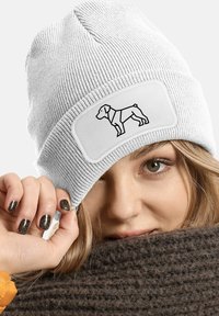 White ribbed knit beanie featuring a rectangular patch with a black outline of a dog. Textured fabric, snug fit, and rolled brim.