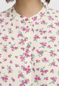 Květinová blůza s krémovým pozadím, zdobená vzorem růžových květin a zelených listů. Růžové knoflíky podél přední části a kulatý límec.