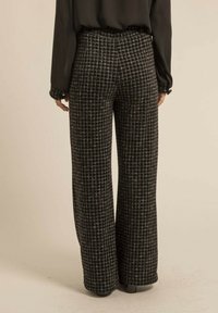 Pantalon large à motif à carreaux noir et blanc. Tissu texturé avec coupe ajustée, taille haute et détail de poignet discret.