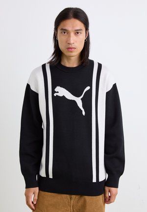 Sort og hvid strikket sweater med et fremtrædende Puma-logo, vertikalt stribedesign, rund hals og ribbestrikkede manchetter og kant.
