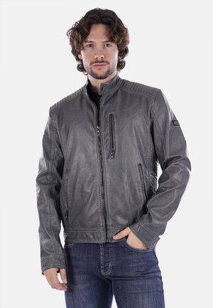 Giacca in pelle grigia con colletto alto, zip frontale, tasche laterali e dettagli testurizzati sulle spalle. Indossata sopra una maglietta nera e jeans.