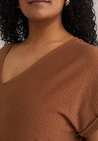 Haut marron à col en V en tissu doux et texturé avec de petits points surélevés ; manches courtes et coupe décontractée.