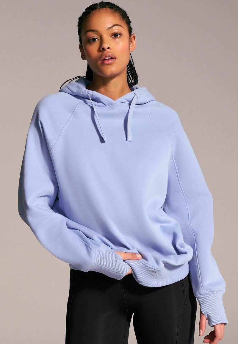 Ljus lavendelfärgad hoodie med dragsko i huvan, ribbade ärmslut och avslappnad passform, tillsammans med svarta leggings. Tyget verkar slätt och mjukt.