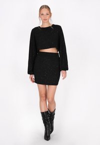Schwarzes, kurzes Langarmoberteil und passender Minirock mit glitzernder Textur. Getragen mit knielangen schwarzen Stiefeln, die eine figurbetonte Silhouette betonen.