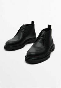 Czarne skórzane botki za kostkę z okrągłym noskiem, sznurowanym przodem i grubą, teksturowaną podeszwą. Charakteryzują się prostym wzornictwem oraz pętelką z tyłu.