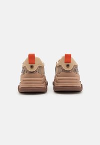 Baskets de sport marron et beige avec un dessus en mesh, une semelle rembourrée, une languette de talon orange et des accents en caoutchouc proéminents.