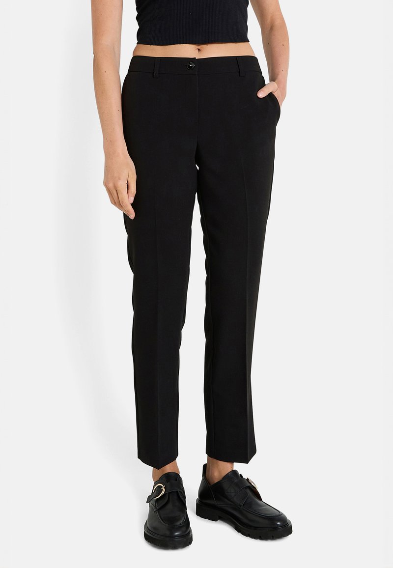 Pantalones negros a medida con una cintura ajustada, frente plano, bolsillos laterales y un largo recortado hasta el tobillo. Combínalos con zapatos negros de deslizar.