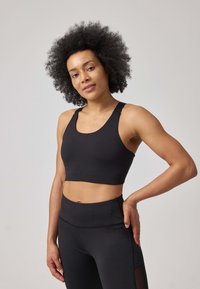 Sostegno sportivo nero con spalline larghe, design corto e texture liscia. Abbinato a leggings neri a vita alta con dettagli in rete.