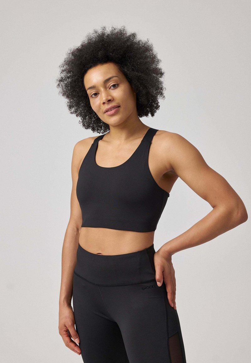 Sostegno sportivo nero con spalline larghe, design corto e texture liscia. Abbinato a leggings neri a vita alta con dettagli in rete.