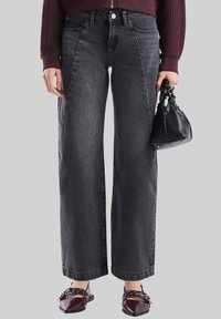 Jeans in denim nero a vita alta e gamba larga con una leggera texture, design a cinque tasche e chiusura frontale con bottone.